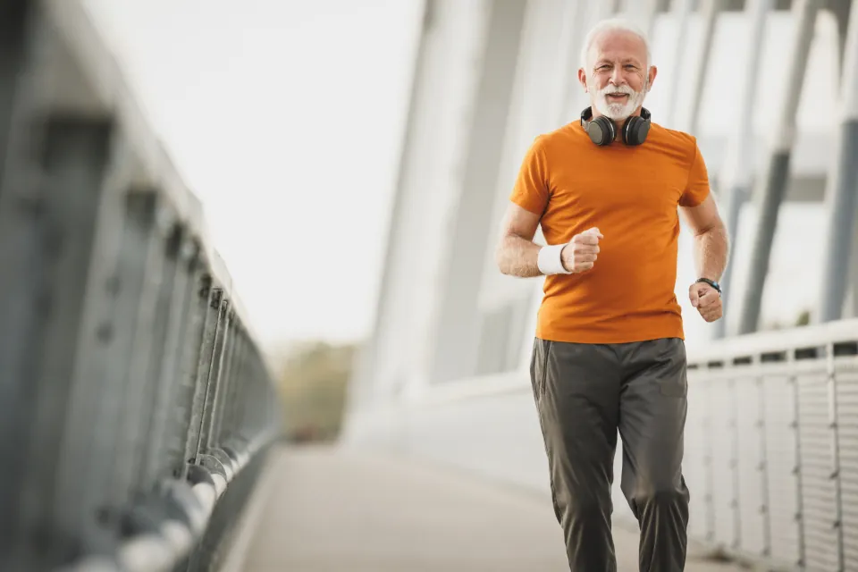 Homme senior en t-shirt orange faisant son jogging sur une passerelle